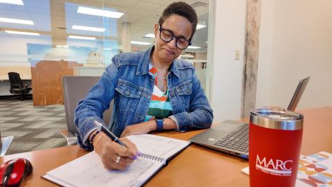 Person writing on planner with a laptop and MARC water container