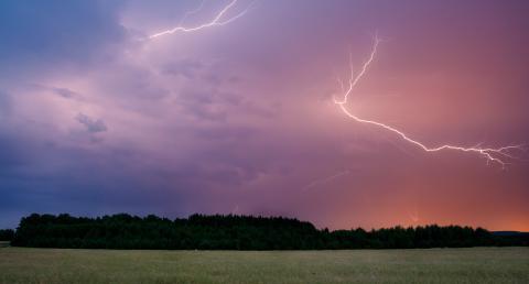 A bolt of lightning in the sky as a thunderstorm rolls across a field
