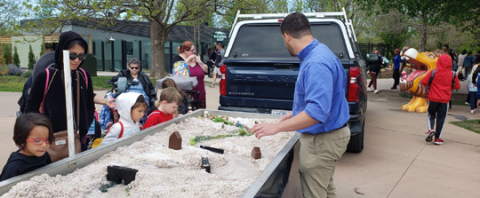 Instructor showcases water flowing through small channels in a diorama outdoors as children watch